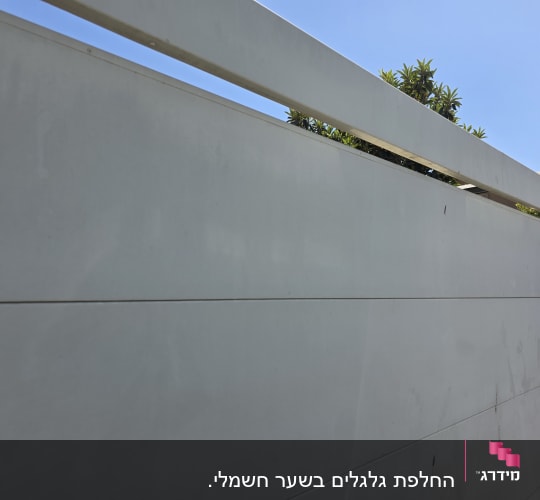 שער חשמלי לבן עם שמיים כחולים ועצים ברקע